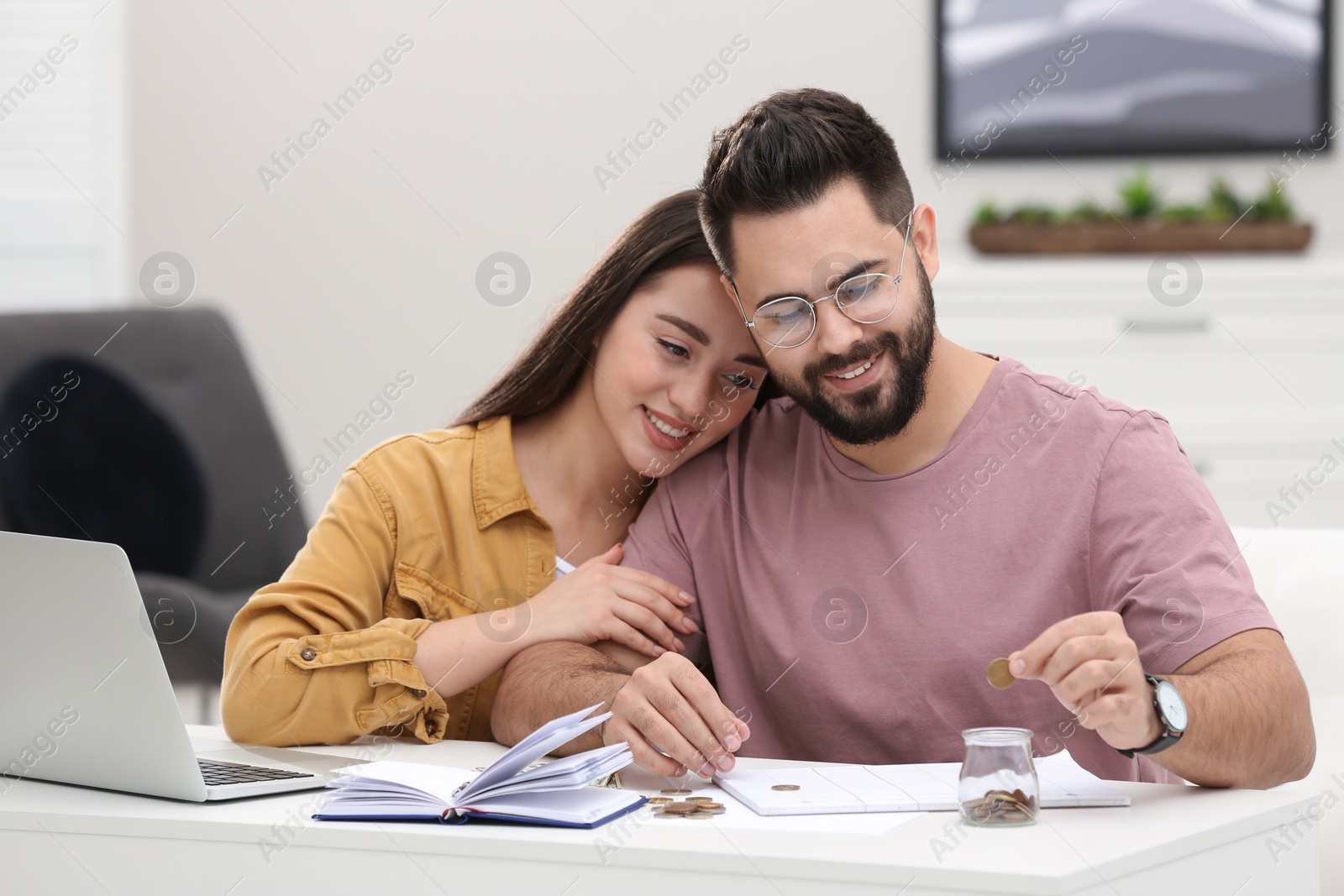 Photo of Happy young couple counting money at white table indoors