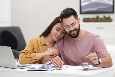 Photo of Happy young couple counting money at white table indoors