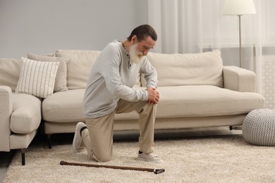 Photo of Senior man with walking cane suffering from knee pain at home. Rheumatism symptom