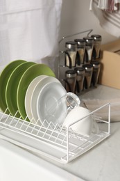 Drainer with different clean dishware, glass and cup on white table indoors