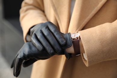 Photo of Woman in stylish leather gloves checking time outdoors, closeup of hands