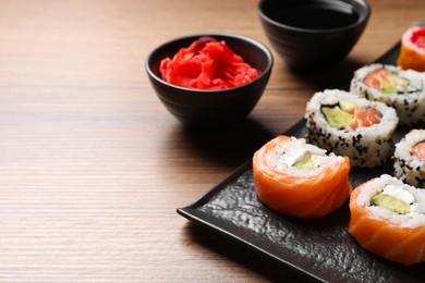 Photo of Delicious sushi rolls, soy sauce and ginger on wooden table, space for text