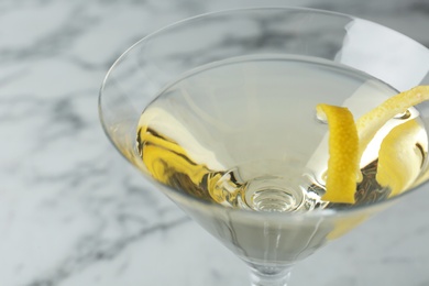 Photo of Glass of lemon drop martini cocktail with zest on marble table, closeup