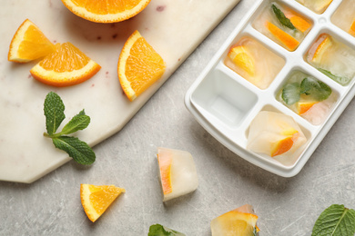Photo of Ice cubes in tray with orange slices and mint on light grey table, flat lay