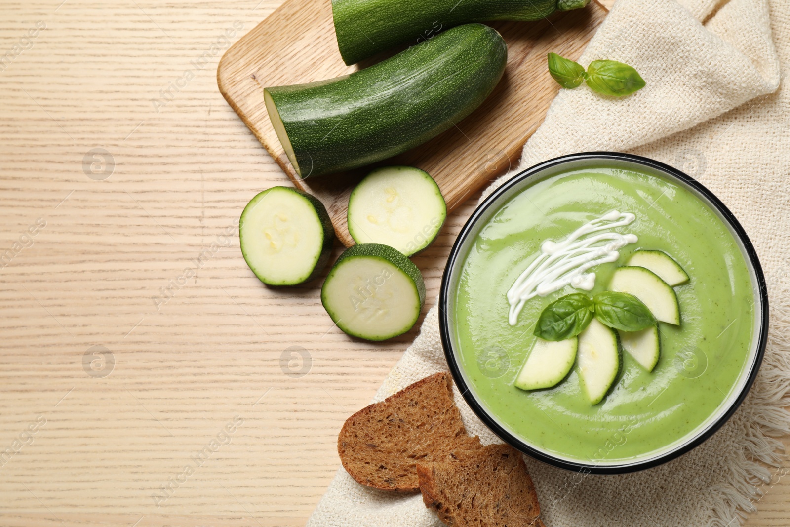 Photo of Tasty homemade zucchini cream soup served on wooden table, flat lay