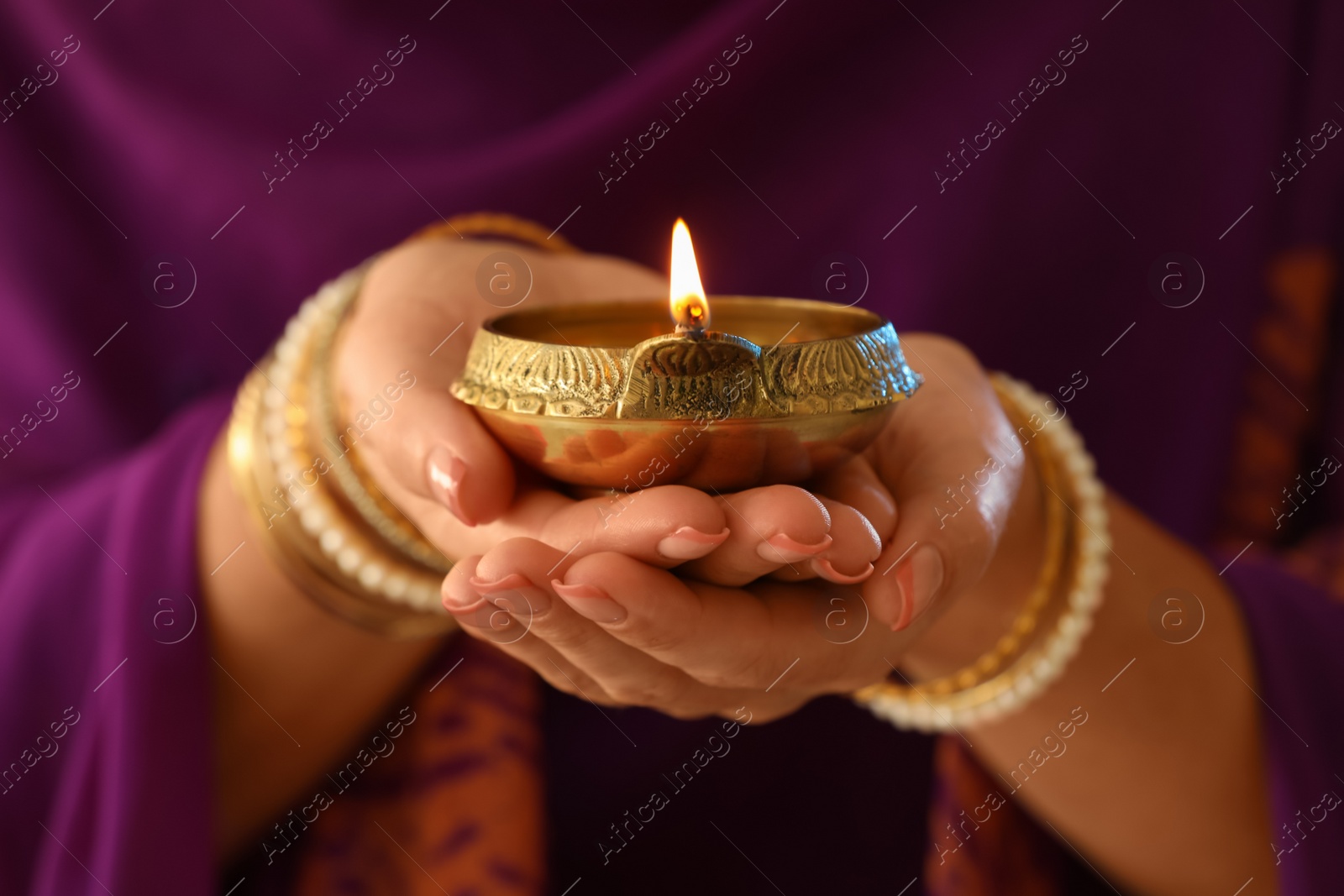 Photo of Woman holding lit diya lamp in hands, closeup. Diwali celebration