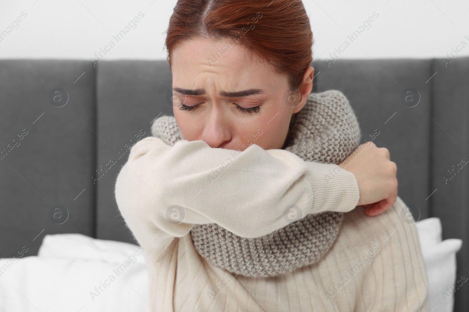 Photo of Woman with scarf coughing on bed. Cold symptoms