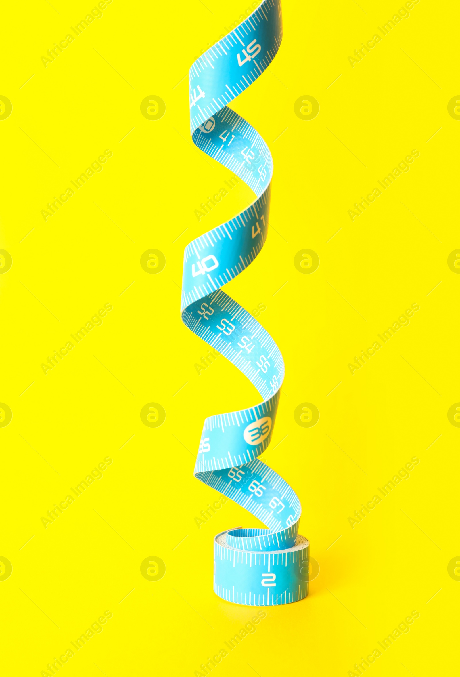 Photo of Light blue measuring tape on yellow background, closeup