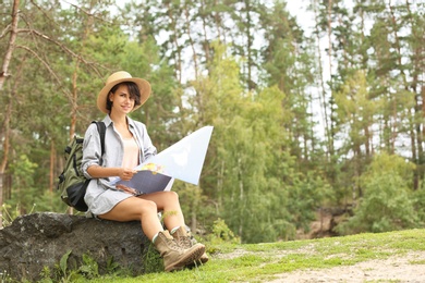 Young woman with map sitting on rock in forest. Camping season