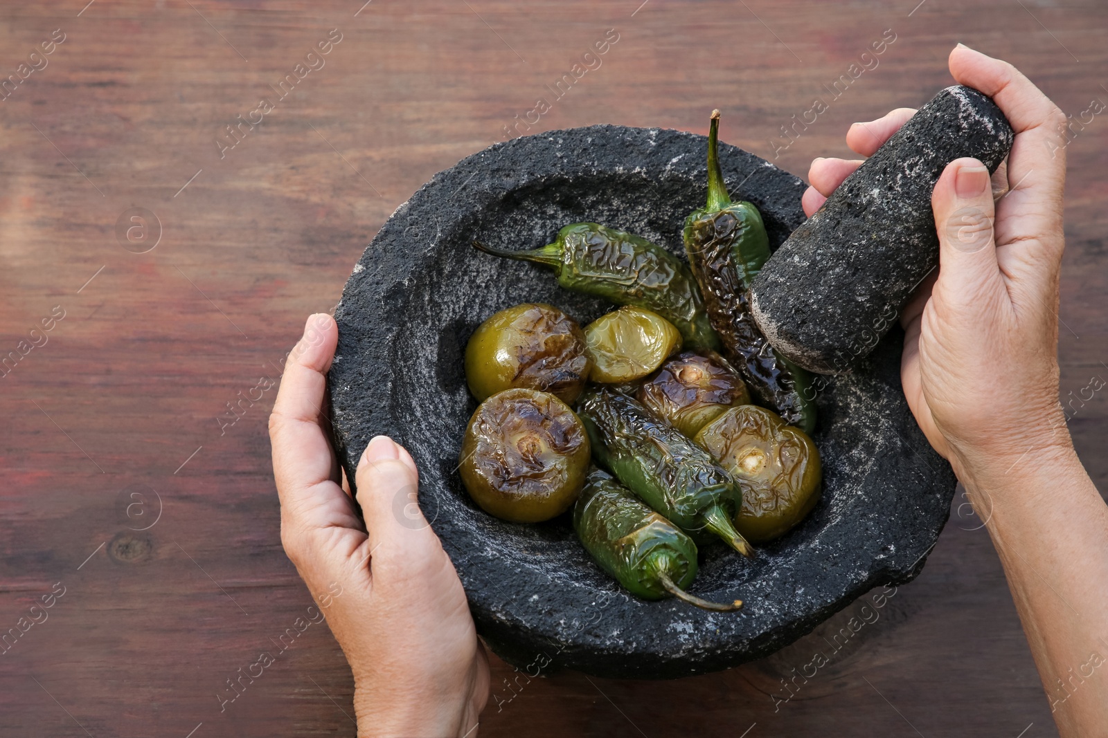 Photo of Woman grinding vegetables in mortar at wooden table, above view. Ingredients for salsa sauce