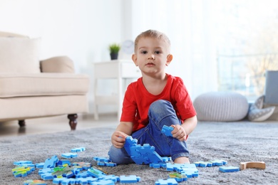 Cute little child playing with puzzles on floor indoors