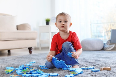 Photo of Cute little child playing with puzzles on floor indoors