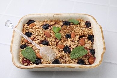 Photo of Tasty baked oatmeal with berries, almonds and honey dipper in baking tray on white table, closeup