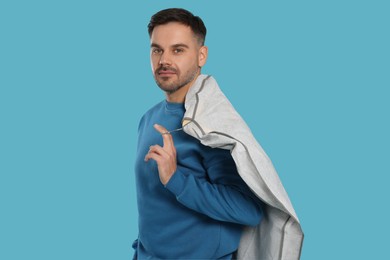 Photo of Man holding garment cover with clothes on light blue background. Dry-cleaning service