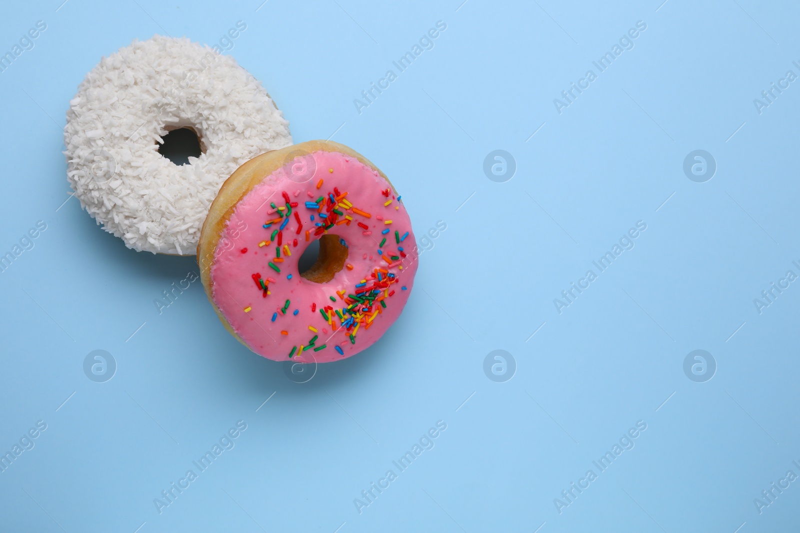 Photo of Tasty glazed donuts decorated with coconut shavings and sprinkles on light blue background, flat lay. Space for text