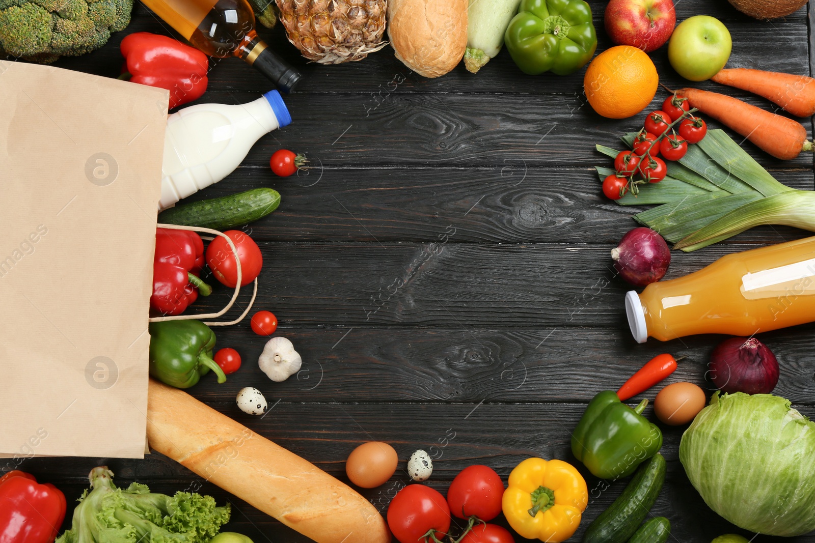 Photo of Frame made with overturned paper bag and groceries on black wooden background, top view. Space for text