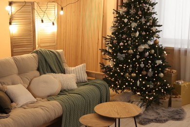 Photo of Comfortable sofa and coffee table near Christmas tree in room