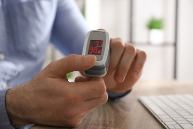 Photo of Man measuring oxygen level with modern fingertip pulse oximeter at workplace, closeup