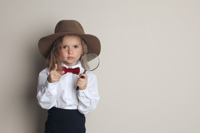 Photo of Cute little child in hat with magnifying glass playing detective on beige background, space for text