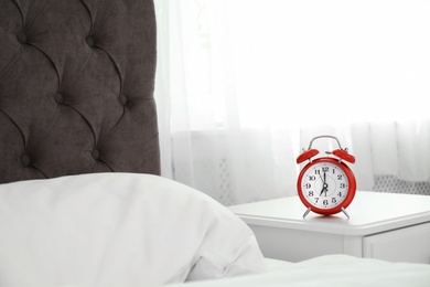 Photo of Analog alarm clock on table in bedroom. Time of day