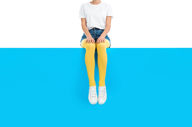 Woman wearing yellow tights and stylish shoes sitting on color background, closeup