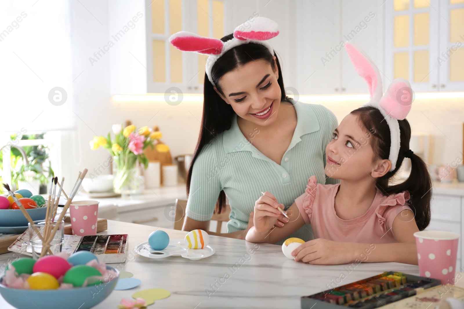 Photo of Happy mother with her cute daughter painting Easter eggs at table in kitchen