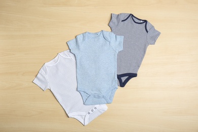 Photo of Different baby bodysuits on wooden background, top view