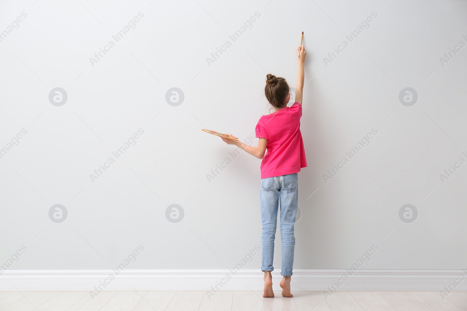 Photo of Little girl painting on light wall indoors, back view. Space for text