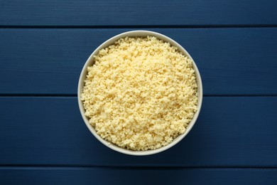 Photo of Bowl of tasty couscous on blue wooden table, top view