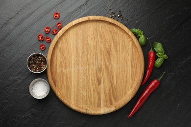 Photo of Cutting board, salt, spices, basil and chili peppers on black textured table, flat lay. Space for text