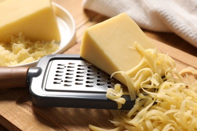 Photo of Grated, whole piece of cheese and grater on table, closeup