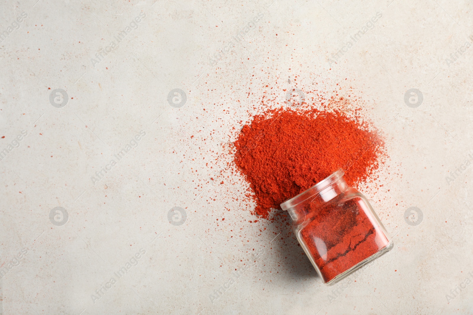 Photo of Glass jar with powdered red chili pepper and space for text on light background, top view