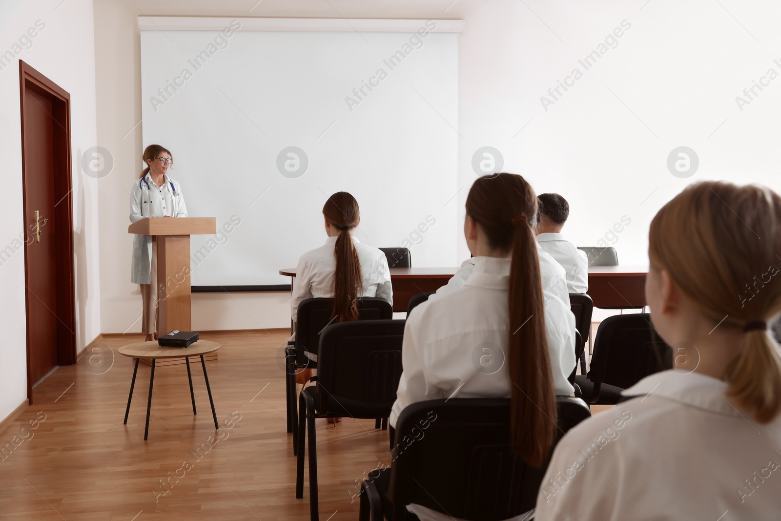 Photo of Doctor giving lecture in conference room with projection screen