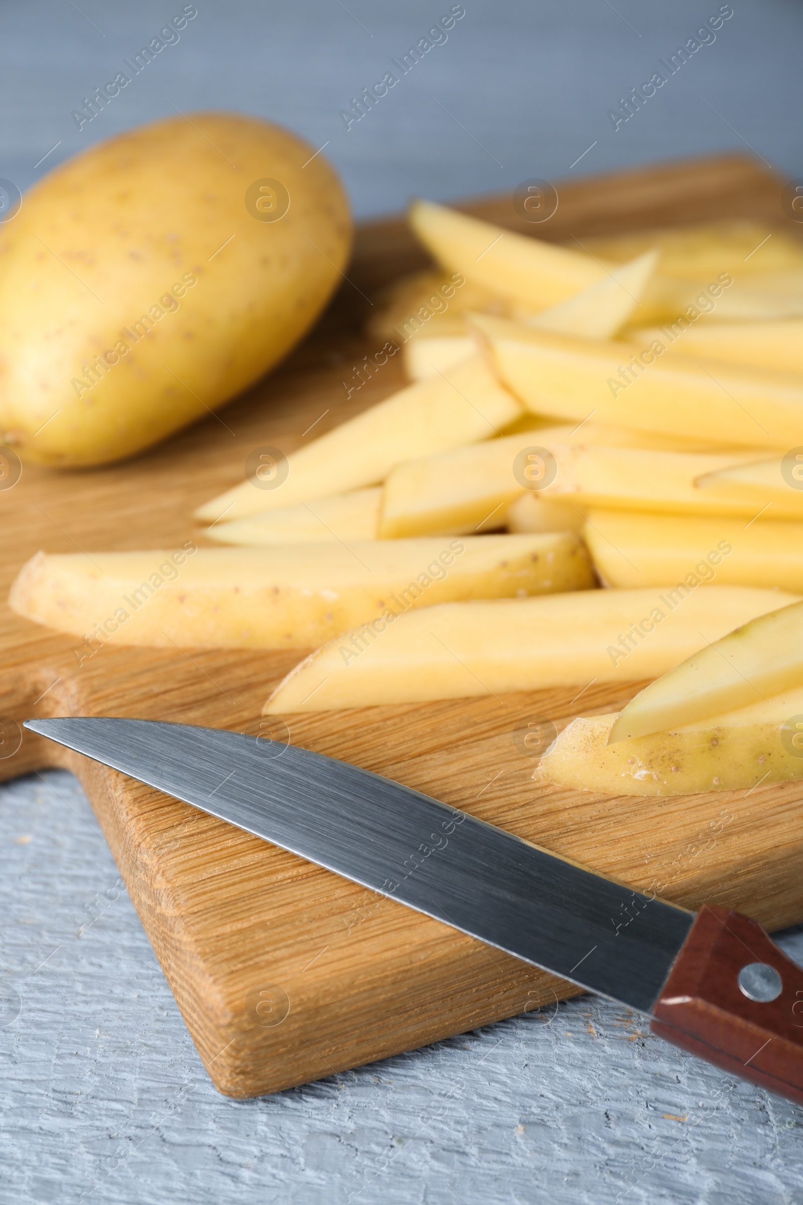 Photo of Whole and cut potatoes with knife on grey wooden table, closeup. Cooking delicious french fries