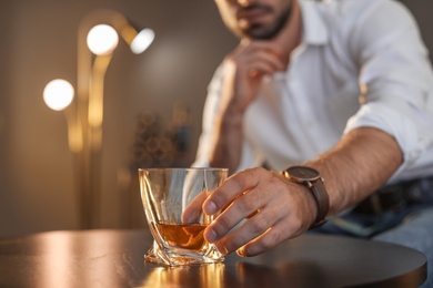 Photo of Man sitting at table with glass of whiskey, closeup. Space for text