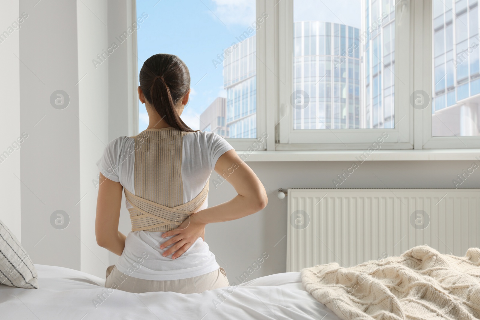 Photo of Woman with orthopedic corset sitting in bedroom, back view