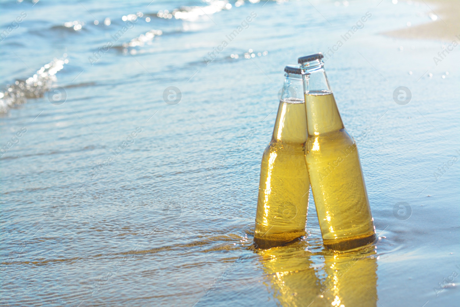 Photo of Bottles of cold beer on sandy beach near sea, space for text