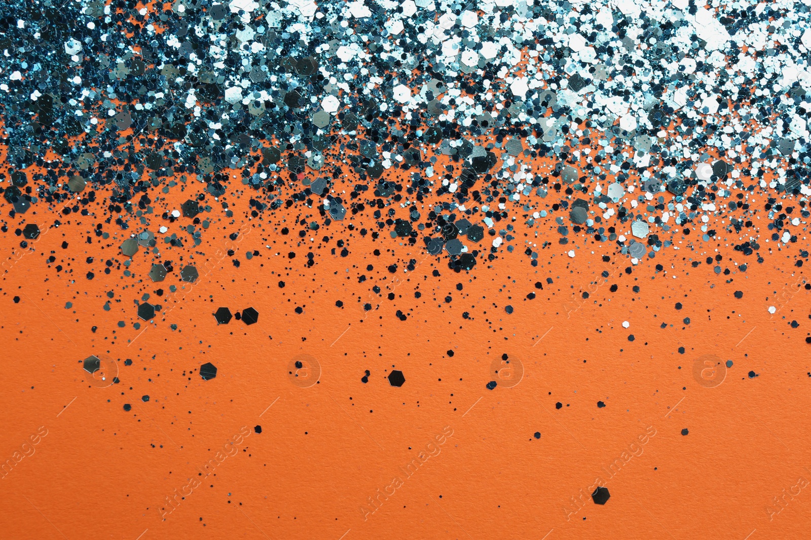 Photo of Shiny bright blue glitter on orange background. Space for text