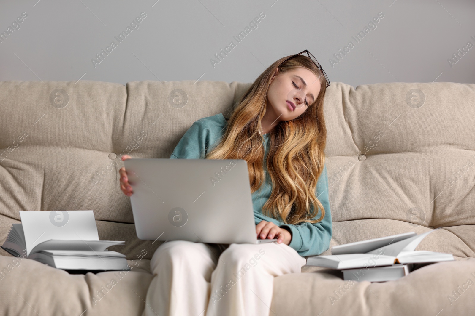 Photo of Young tired woman sleeping with laptop and books on couch at home