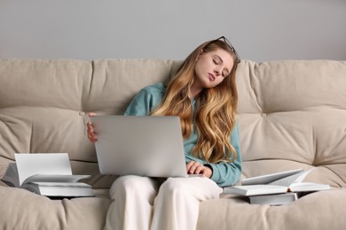 Young tired woman sleeping with laptop and books on couch at home