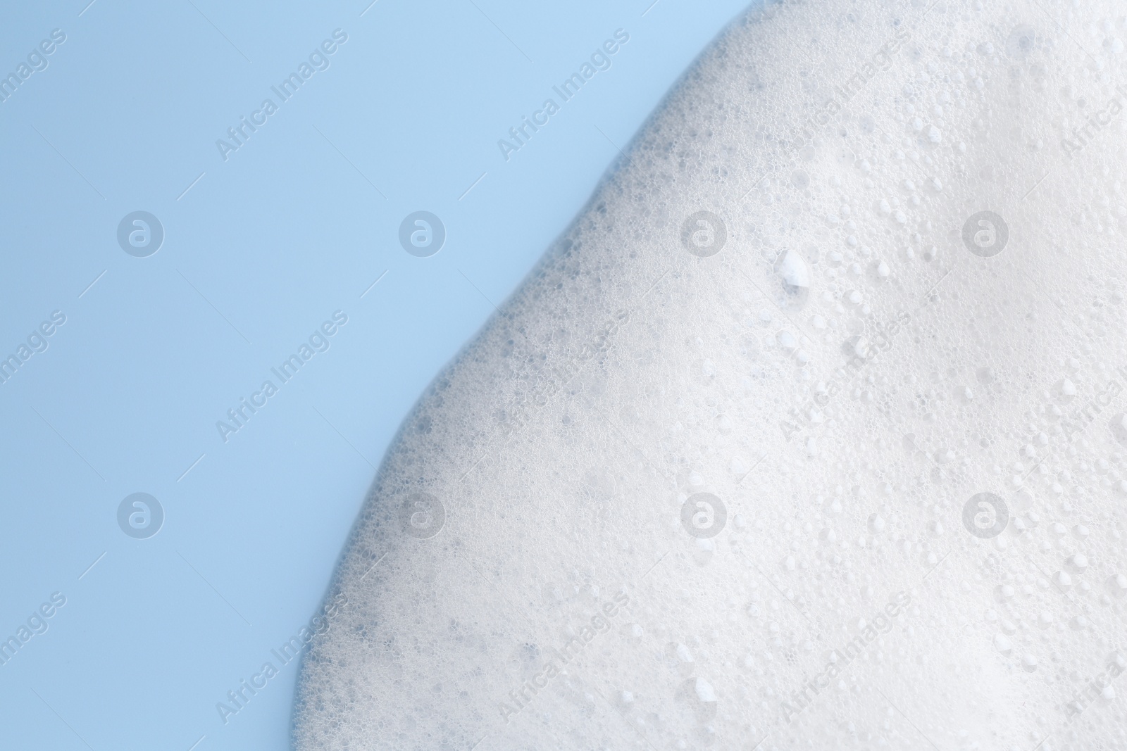 Photo of White fluffy foam on light blue background, top view. Space for text