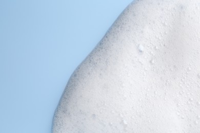 Photo of White fluffy foam on light blue background, top view. Space for text