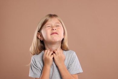 Photo of Suffering from allergy. Little girl scratching her neck on light brown background