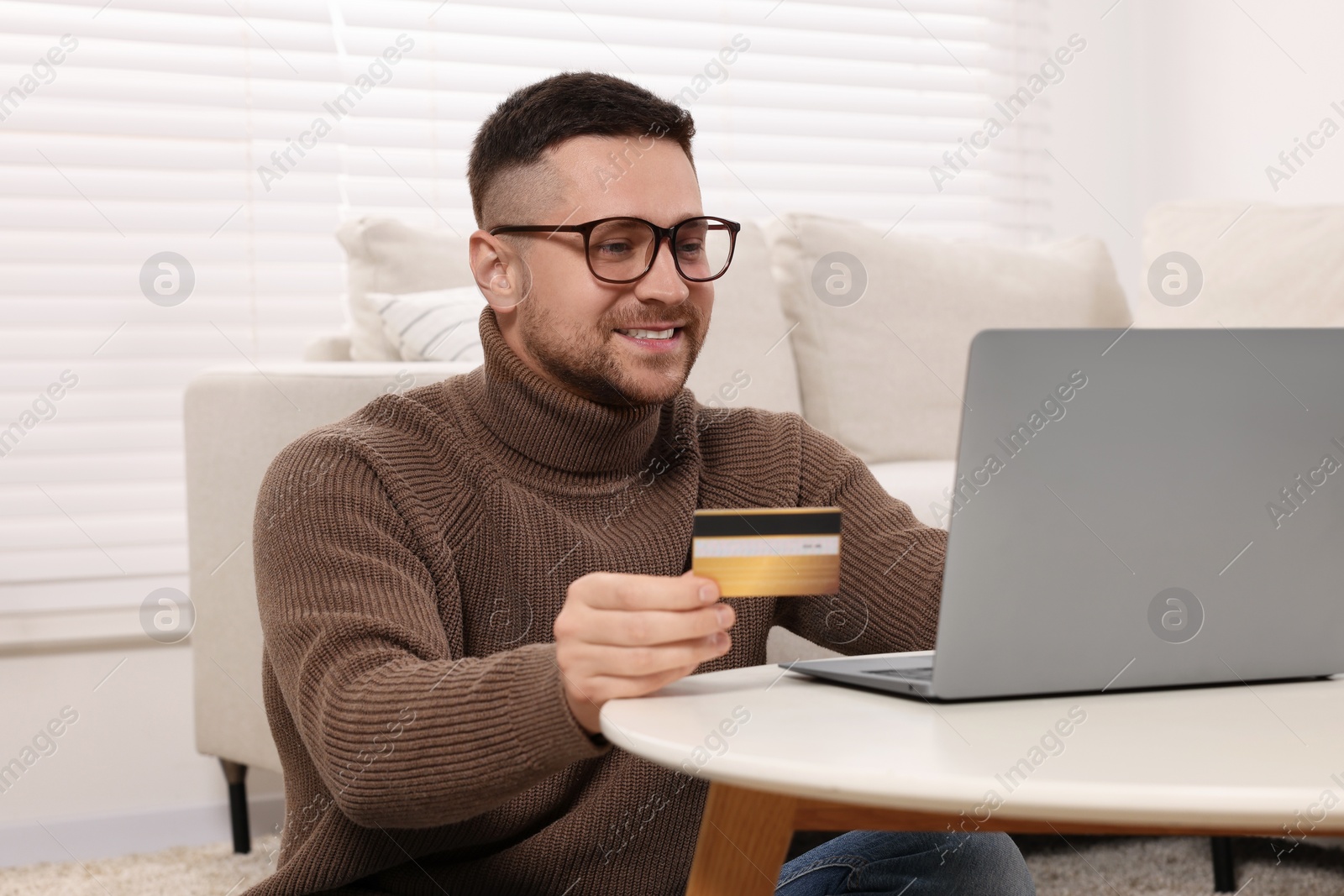 Photo of Handsome man with credit card using laptop for online shopping at home