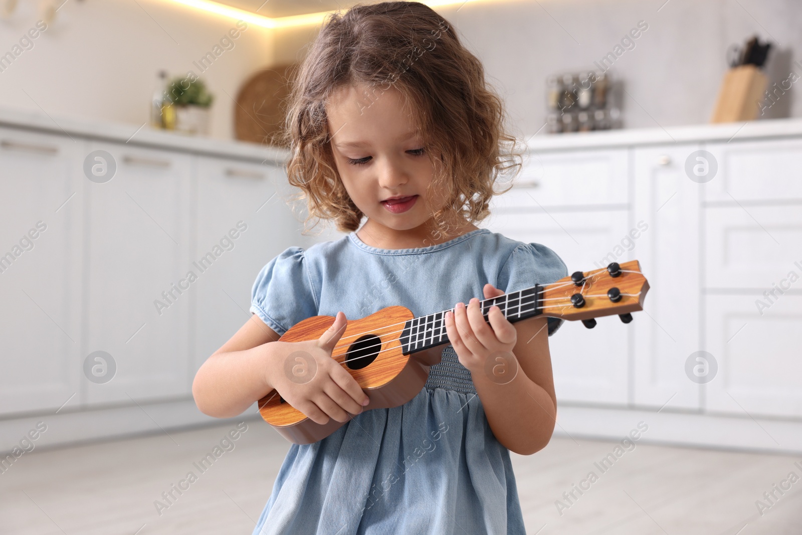 Photo of Little girl playing toy guitar in kitchen