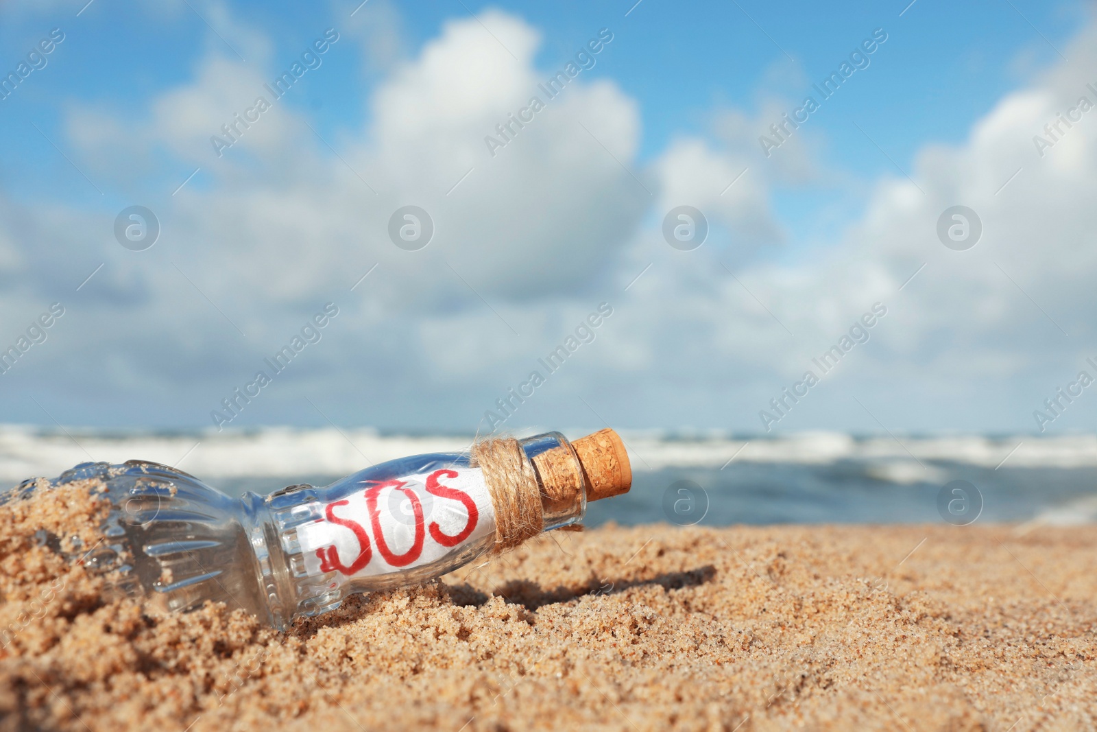 Photo of Glass bottle with SOS message on sand near sea, space for text