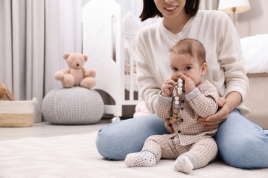 Photo of Young mother and her baby with teether on floor at home. Space for text
