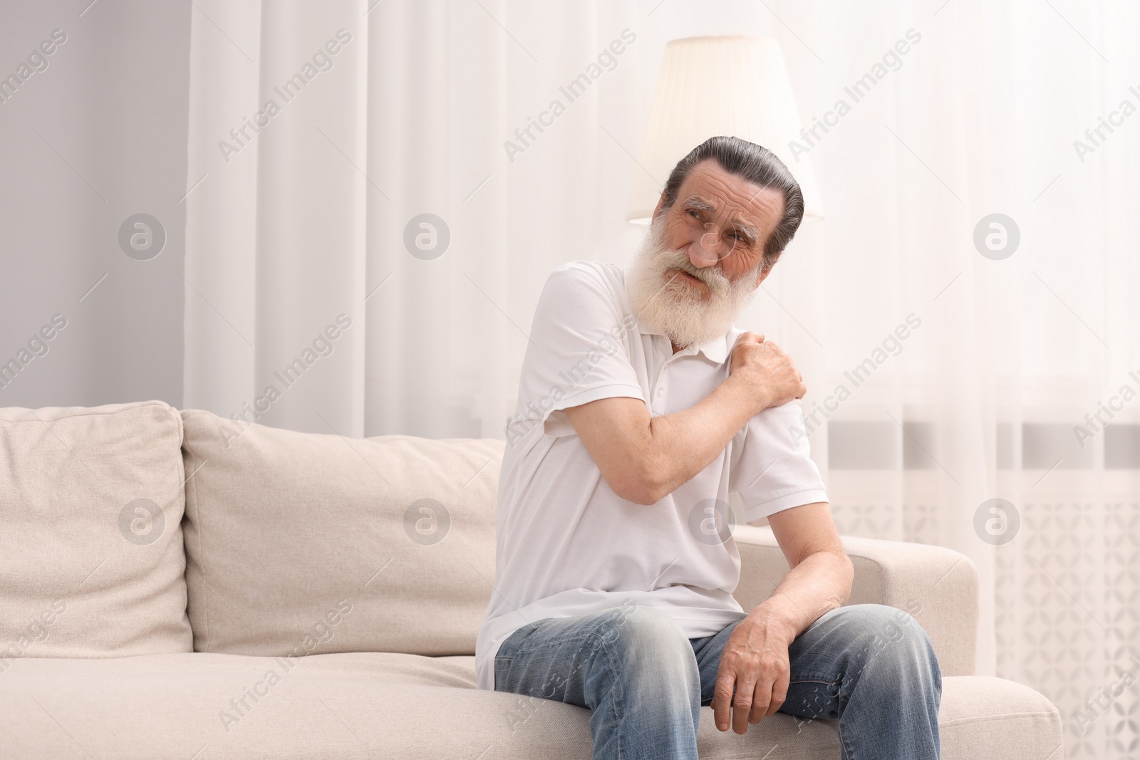 Photo of Senior man suffering from pain in shoulder at home. Rheumatism symptom