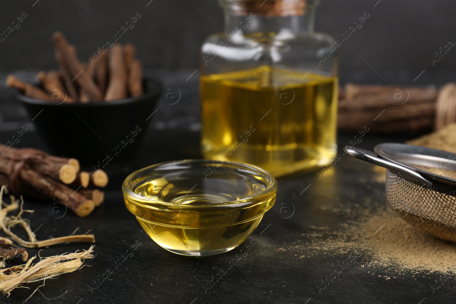 Photo of Bowl with essential oil and dried sticks of liquorice root on black table