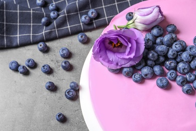 Photo of Tasty blueberry cake decorated with fresh flowers on grey table, closeup. Space for text